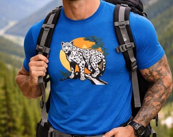 Könnte beinhalten: Ein leuchtend blaues Kurzarm-T-Shirt mit einem Grafikdruck eines weiß-schwarz gefleckten Leoparden, der auf einem Ast vor einer großen gelben kreisförmigen Sonne sitzt, getragen mit einem schwarzen Wanderrucksack.