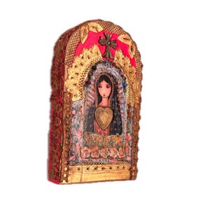 K&ouml;nnte beinhalten: Ein dekorativer, gew&ouml;lbter Wandbehang mit einem zentralen Bild einer Frau mit einem herzf&ouml;rmigen Anh&auml;nger. Das Kunstwerk ist mit Goldfiligran, einem Messingkreuz und einem leuchtend rosa Hintergrund gerahmt. Das St&uuml;ck hat ein strukturiertes, Mixed-Media-Aussehen.