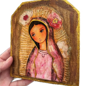 Könnte beinhalten: Religiöse Ikone mit einer Frau in rosa Kleid und Schleier, verziert mit Blumen. Das Kunstwerk hat einen goldenen Rand und Hintergrund mit strukturierter Oberfläche. Das Bild wird von einer Hand gehalten.