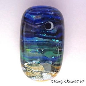 May include: A blue and green glass bead with a white crescent moon design. The bead has a layered effect, with a gold and white layer at the bottom.