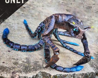 May include: A detailed, articulated model of a creature with a segmented body, multiple limbs, and a head with glowing blue eyes. The model is primarily brown and blue, with accents of teal and yellow. The text "DIGITAL FILE ONLY" is visible.