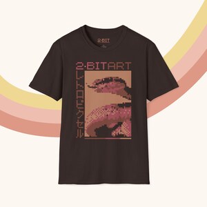 Op de afbeelding: Donkerbruin t-shirt met een gepixeld slangengrafisch en de tekst "2-BITART" en Japanse karakters. Het shirt heeft een ronde hals en korte mouwen. De merknaam "2-BIT" staat in het midden bovenaan.