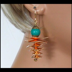 May include: Gold dangle earrings with a turquoise and orange bead and layered copper-colored metal pieces.