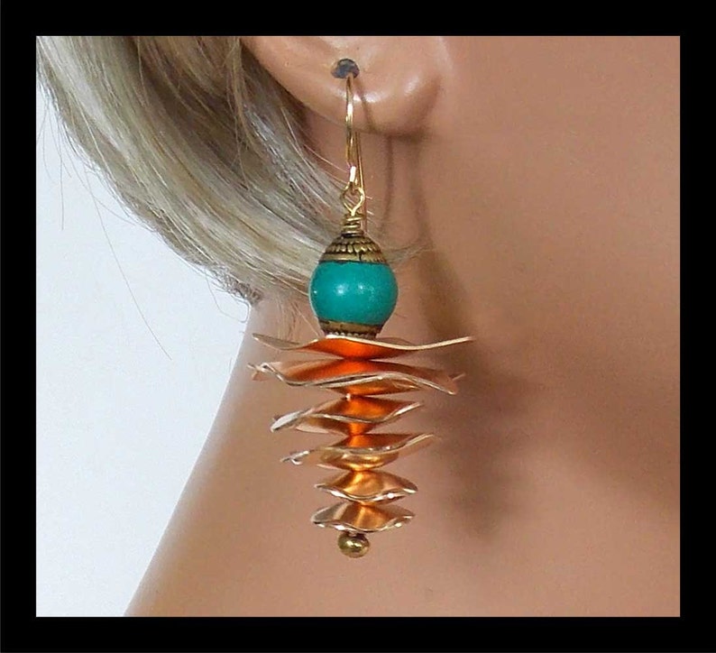 May include: Gold dangle earrings with a turquoise and orange bead and layered copper-colored metal pieces.