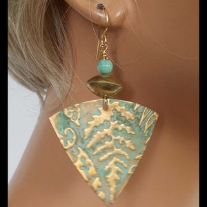 May include: Triangle-shaped earrings with a gold and green patina finish. The earrings feature a small turquoise bead and a gold disc.