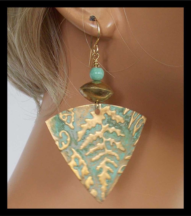 May include: Triangle-shaped earrings with a gold and green patina finish. The earrings feature a small turquoise bead and a gold disc.