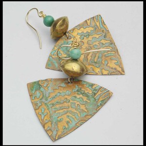 May include: A pair of gold-toned earrings with a triangular shape and a textured surface. The earrings feature a turquoise bead and a gold-toned bead.