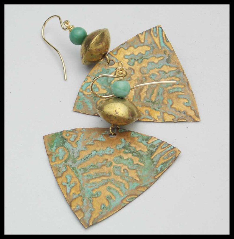May include: A pair of gold-toned earrings with a triangular shape and a textured surface. The earrings feature a turquoise bead and a gold-toned bead.