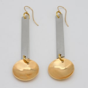 May include: A pair of silver and gold earrings with a long, rectangular bar and a round, gold disc at the bottom.