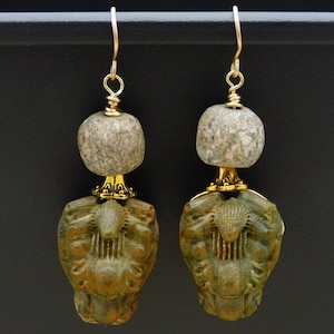 May include: A pair of gold earrings with a green stone and a grey stone. The green stone is carved with a design of a lyre and a figure.