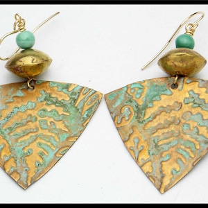 May include: A pair of gold earrings with a triangular shape and a textured surface. The earrings have a green bead at the top of each earring.