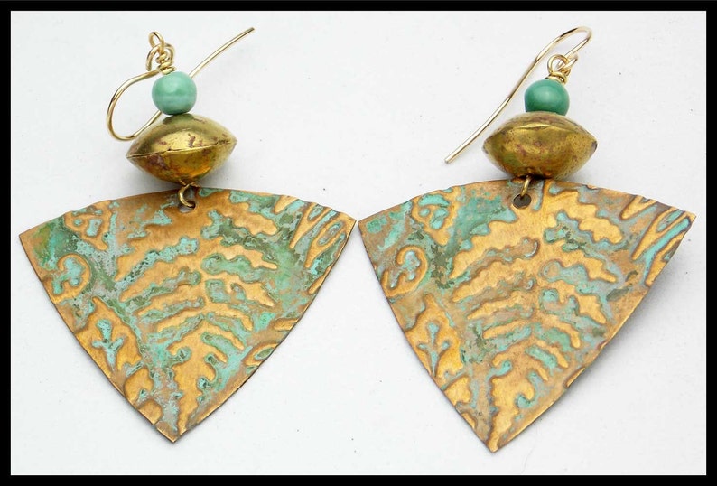 May include: A pair of gold earrings with a triangular shape and a textured surface. The earrings have a green bead at the top of each earring.