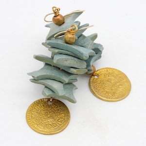 Könnte beinhalten: Ein Paar Ohrringe aus gestapelten blauen Keramikteilen mit goldenen Akzenten. Jeder Ohrring hat einen goldenen Münzenanhänger mit arabischer Schrift.