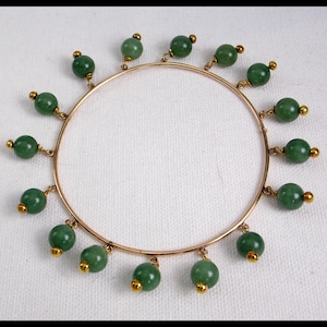May include: A gold bangle bracelet with dangling green jade beads.