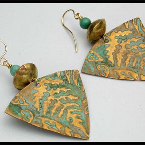 May include: A pair of gold earrings with a triangular pendant featuring a textured, green and gold design. Each earring has a small, round, green bead and a gold bead.
