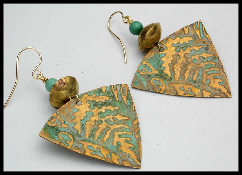 May include: A pair of gold earrings with a triangular pendant featuring a textured, green and gold design. Each earring has a small, round, green bead and a gold bead.
