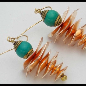 May include: A pair of gold earrings with turquoise beads and a layered copper design. The earrings are made of metal and have a unique, geometric shape.