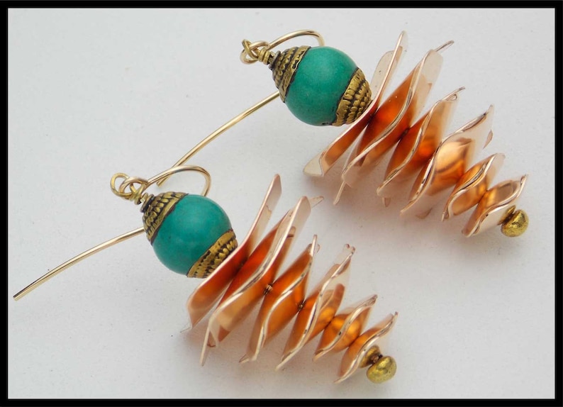 May include: A pair of gold earrings with turquoise beads and a layered copper design. The earrings are made of metal and have a unique, geometric shape.