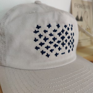 May include: A light gray baseball cap with a navy blue embroidered design of a grid of plus signs.