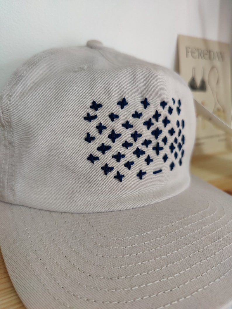 May include: A light gray baseball cap with a navy blue embroidered design of a grid of plus signs.