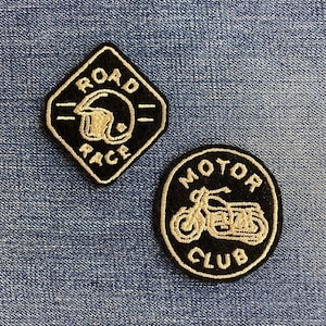 Pode incluir: Dois patches bordados em ganga. Um é um losango preto com "ROAD RACE" e um desenho de capacete em branco. O outro é um círculo preto com uma motocicleta e "MOTOR CLUB" em branco.