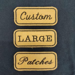 Puede incluir: Tres parches rectangulares amarillos con bordes y texto negros. El parche superior dice "Custom", el parche central dice "LARGE" y el parche inferior dice "Patches". Los parches están sobre una tela azul oscuro.