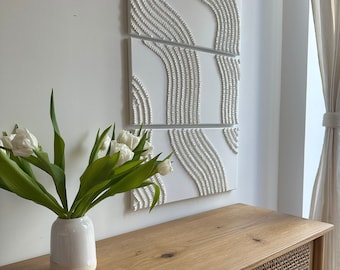 May include: A white wooden cabinet with two doors featuring a woven rattan design. The cabinet is topped with a light wood surface and a white vase with white flowers.