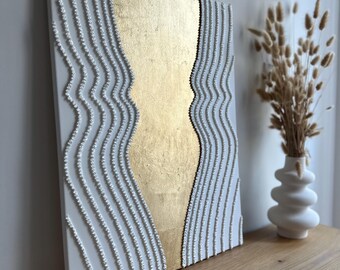 May include: Abstract wall art with white textured lines and a gold background. The lines are made of small white beads and create a wavy pattern.