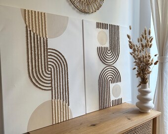 Puede incluir: Dos piezas de arte de pared de lienzo beige con patrones de cuentas marrones y blancas. El arte está colgado en una pared blanca sobre un gabinete de madera con puertas de ratán tejido. Dos piezas de decoración de pared de ratán tejido están colgadas sobre el arte.
