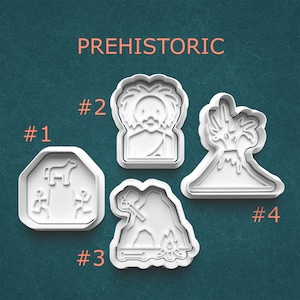 May include: Four white plastic cookie cutters with a prehistoric theme. The cutters include a cave painting, a caveman, a cave with a fire, and a volcano. The word "PREHISTORIC" is printed in orange.