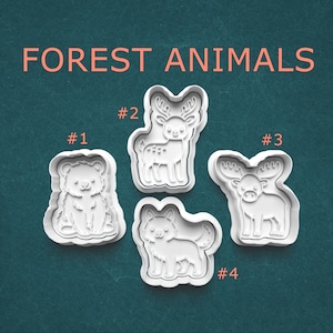 May include: Four white plastic cookie cutters in the shapes of forest animals: a bear, a deer, a moose, and a fox. The words "FOREST ANIMALS" are in coral-colored text above the cutters. Numbers label each animal.