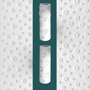 May include: Two white cylindrical rollers featuring a repeating embossed pattern of various sized animal paw prints. The surface of each roller is matte white, displaying a consistent texture of recessed and raised paw print impressions.