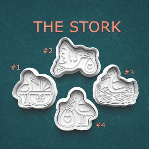May include: Four white plastic cookie cutters labeled with numbers 1 through 4, arranged under the text THE STORK. The designs feature a stork with a baby carriage, a flying stork with a bundle, a stork in a nest, and a stork standing with a bundle.