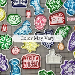 May include: A collection of colorful cookie cutters in various shapes, including a skull, snowflake, and pretzel. The text "Color May Vary" is displayed. These cutters are ideal for baking and crafting.