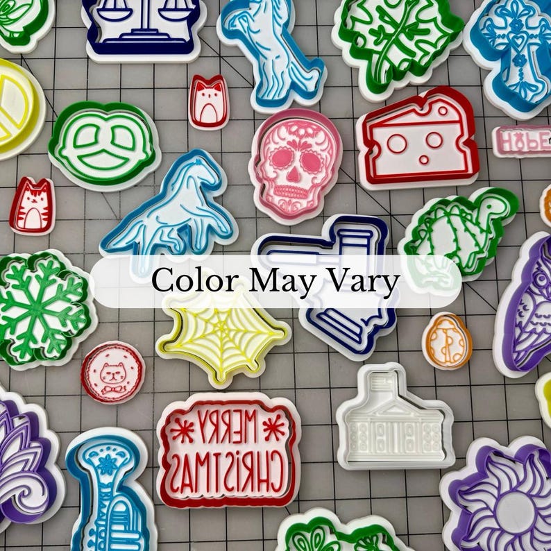 May include: A collection of colorful cookie cutters in various shapes, including a skull, snowflake, and pretzel. The text "Color May Vary" is displayed. These cutters are ideal for baking and crafting.