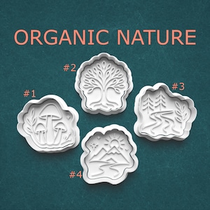 May include: Four white cookie cutters with nature-themed designs: mushrooms, a tree, a river scene with trees, and a mountain landscape. The text "ORGANIC NATURE" is above the cutters. Each cutter is numbered.