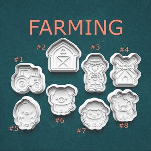 May include: White plastic cookie cutters in various farm shapes, including a tractor, barn, farmer, windmill, chick, pig, sheep, and cow. The word "FARMING" is displayed in orange block letters above the cutters.