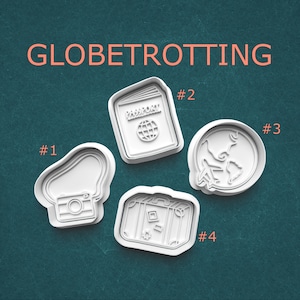 May include: Four white cookie cutters with travel-themed designs. The cutters include a camera, a passport, a globe with an airplane, and a suitcase. The word "GLOBETROTTING" is written in orange above the cutters.