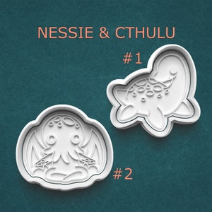 May include: Two white plastic cookie cutters. One is shaped like a stylized Loch Ness Monster, the other like Cthulhu. The text "NESSIE & CTHULU" is above the cutters, with the numbers "#1" and "#2" next to each cutter.