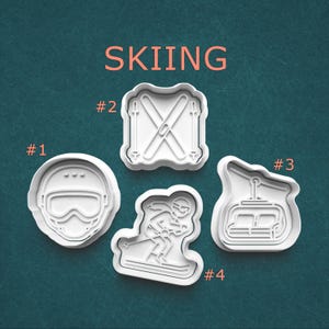 May include: Four white plastic cookie cutters with a skiing theme. The cutters include a ski helmet, skis, a skier, and a ski lift. The word "SKIING" is printed in orange at the top of the image.