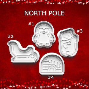 May include: Four white plastic cookie cutters with a North Pole theme. The cutters include a penguin, a sleigh, a bear wearing a scarf, and an igloo. The text "NORTH POLE" is above the cutters.