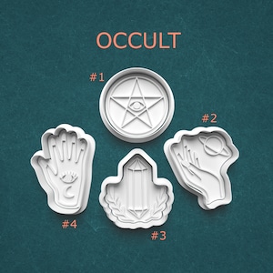 May include: White plastic cookie cutters with occult symbols, including a pentagram with an eye, a hand with an eye and crescent moon, a crystal, and a hand holding a planet. The word "OCCULT" is printed at the top.