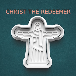 May include: A white plastic cookie cutter in the shape of the Christ the Redeemer statue, with the text "CHRIST THE REDEEMER" in orange above it. The cutter has a detailed outline of the statue's form, with arms outstretched. The background is a teal color.