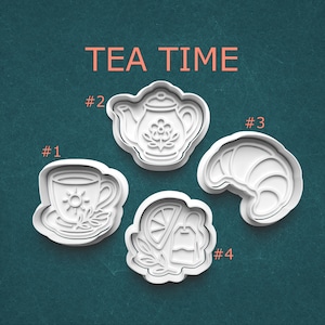 May include: White plastic cookie cutters in the shapes of a teacup, teapot, croissant, and tea bag with lemon and leaves. The words "TEA TIME" are in coral-colored text above the cutters. Numbers are next to each cutter.