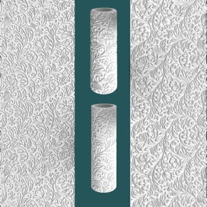 May include: Two white cylindrical paint rollers with floral patterns are displayed against a teal background, flanked by panels of matching floral wallpaper. The rollers and wallpaper feature a raised, embossed design of flowers and leaves.