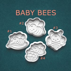 May include: Four white plastic cookie cutters labeled BABY BEES with numbers #1 through #4. Cutter #1 shows a bee on a leaf, #2 a flying bee, #3 a front-facing bee, and #4 a bee on a flower. Each cutter features a raised outline design.