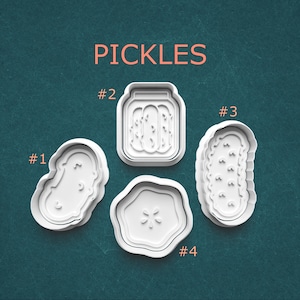 May include: Four white plastic pickle-shaped cookie cutters. The word "PICKLES" is printed in orange above the cutters. The cutters are numbered #1, #2, #3, and #4. The cutters are in the shape of a pickle, a jar of pickles, and a pickle slice.