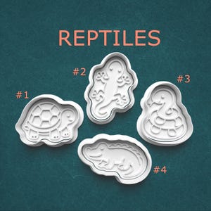 May include: Four white plastic cookie cutters shaped like reptiles, labeled with numbers 1 through 4. The set includes a turtle, a lizard, a snake, and a crocodile. The word REPTILES is printed in large orange letters at the top of the image.