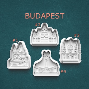 May include: Four white plastic cookie cutters in the shape of Budapest landmarks. The word "BUDAPEST" is printed in orange at the top. Each cutter is numbered from 1 to 4.