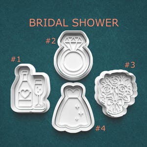 May include: White plastic cookie cutters in the shapes of a champagne bottle and glass, a diamond ring, a wedding dress, and a bouquet of flowers. The text "BRIDAL SHOWER" is above the cutters.